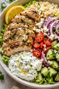sliced grilled chicken with lemon, tomatoes, red onion, cucumber, feta, and dill yogurt sauce in a bowl