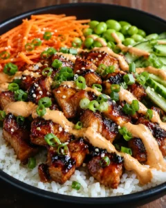 bowl of glossy glazed pork over white rice with shredded carrot, peas, cucumber, scallions, and sesame seeds