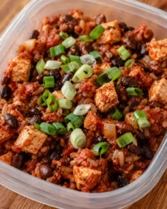 Chili-style mix with beans, tomatoes, cubed white blocks, and sliced green onions in a plastic container.