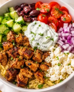 Colorful bowl of Mediterranean chicken with orzo, cucumber, olives, cherry tomatoes, red onion, feta, and tzatziki