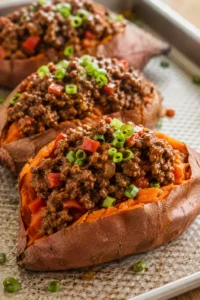 Roasted sweet potatoes halved and loaded with browned ground beef, red peppers, and green onions.