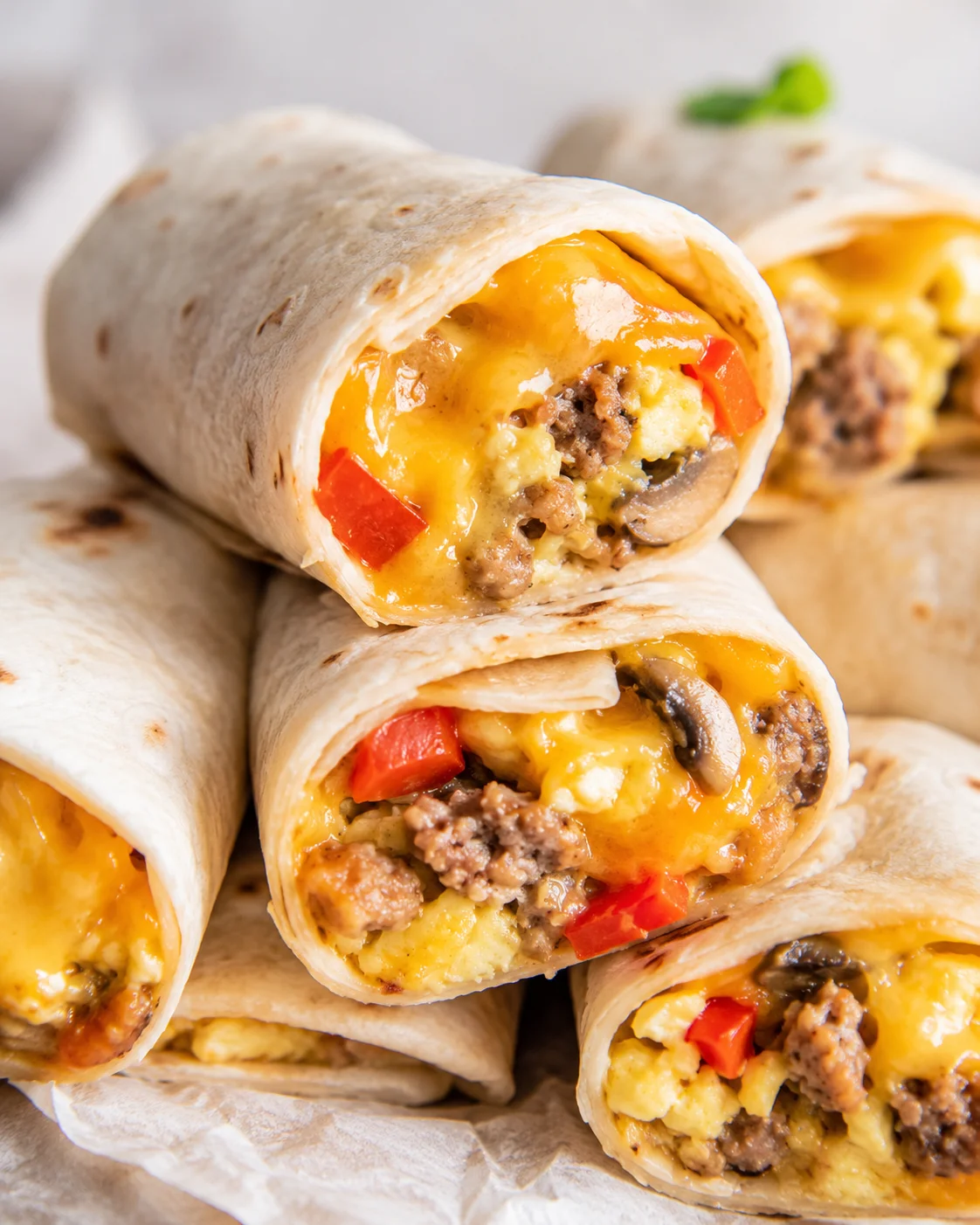 Close-up of stacked breakfast burrito halves with melted cheese and visible sausage and peppers