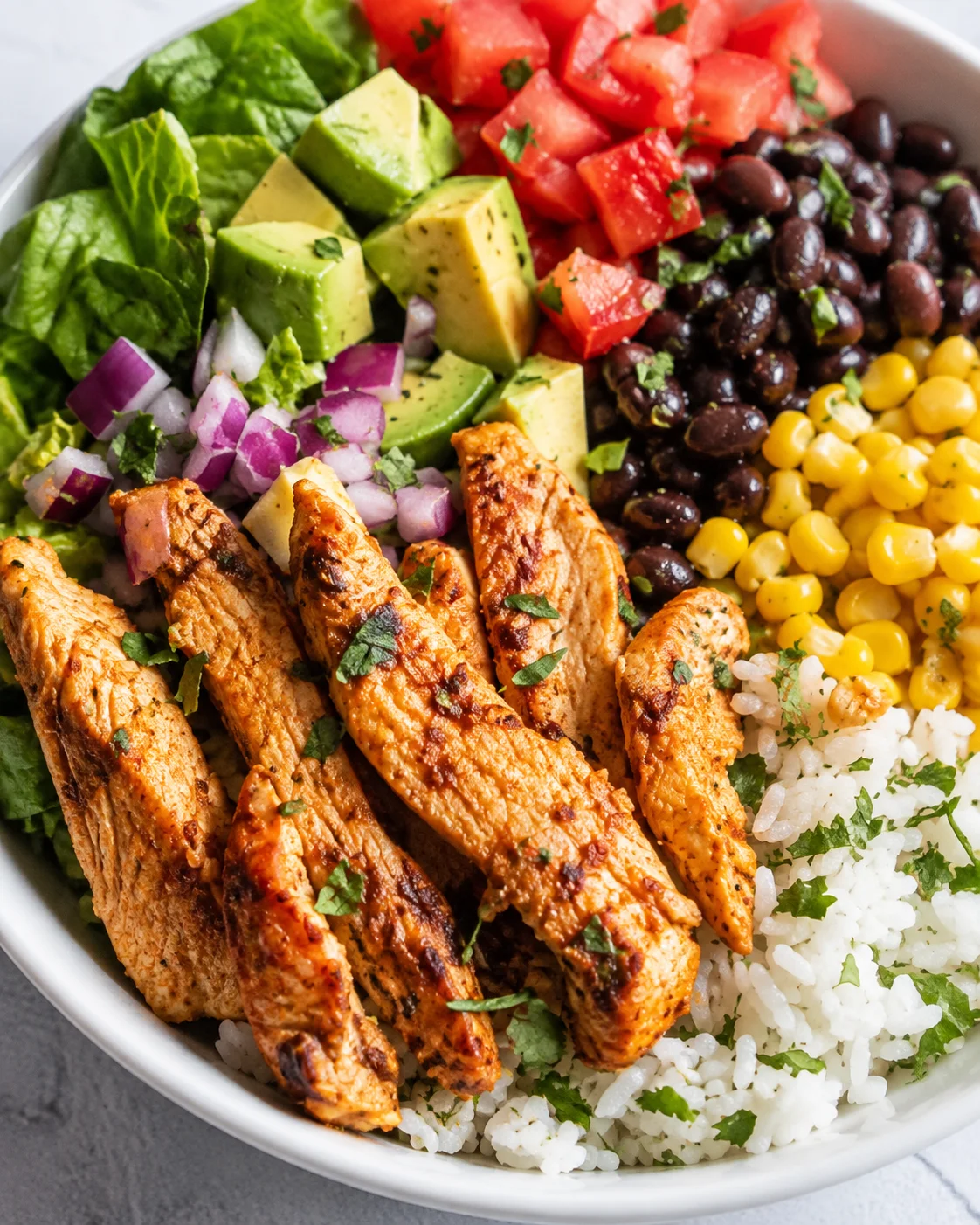 Close-up of Chicken Burrito Bowl showing seared chicken strips, rice, black beans, corn and avocado