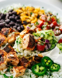 Close-up spoonful of chicken burrito bowl showing rice, seasoned chicken cube, pico and guacamole