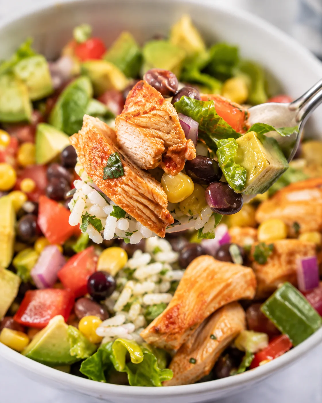 Forkful of Chicken Burrito Bowl with chicken, rice, avocado, corn and black beans