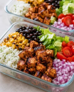 Two glass meal prep containers with chipotle chicken, rice, charred corn, black beans, tomatoes and lettuce
