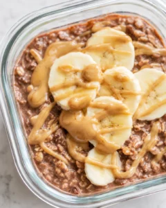 Close-up of chocolate peanut butter overnight oats in a glass container topped with banana slices and drizzled peanut butter