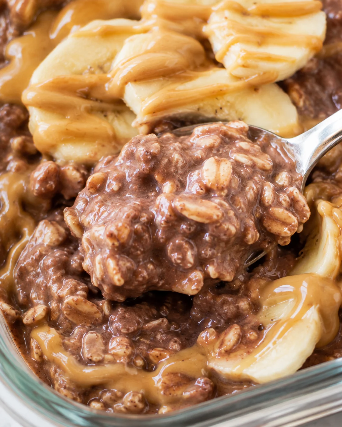 Spoonful close-up of chocolate peanut butter overnight oats showing individual oats and creamy texture with banana and peanut butter in background