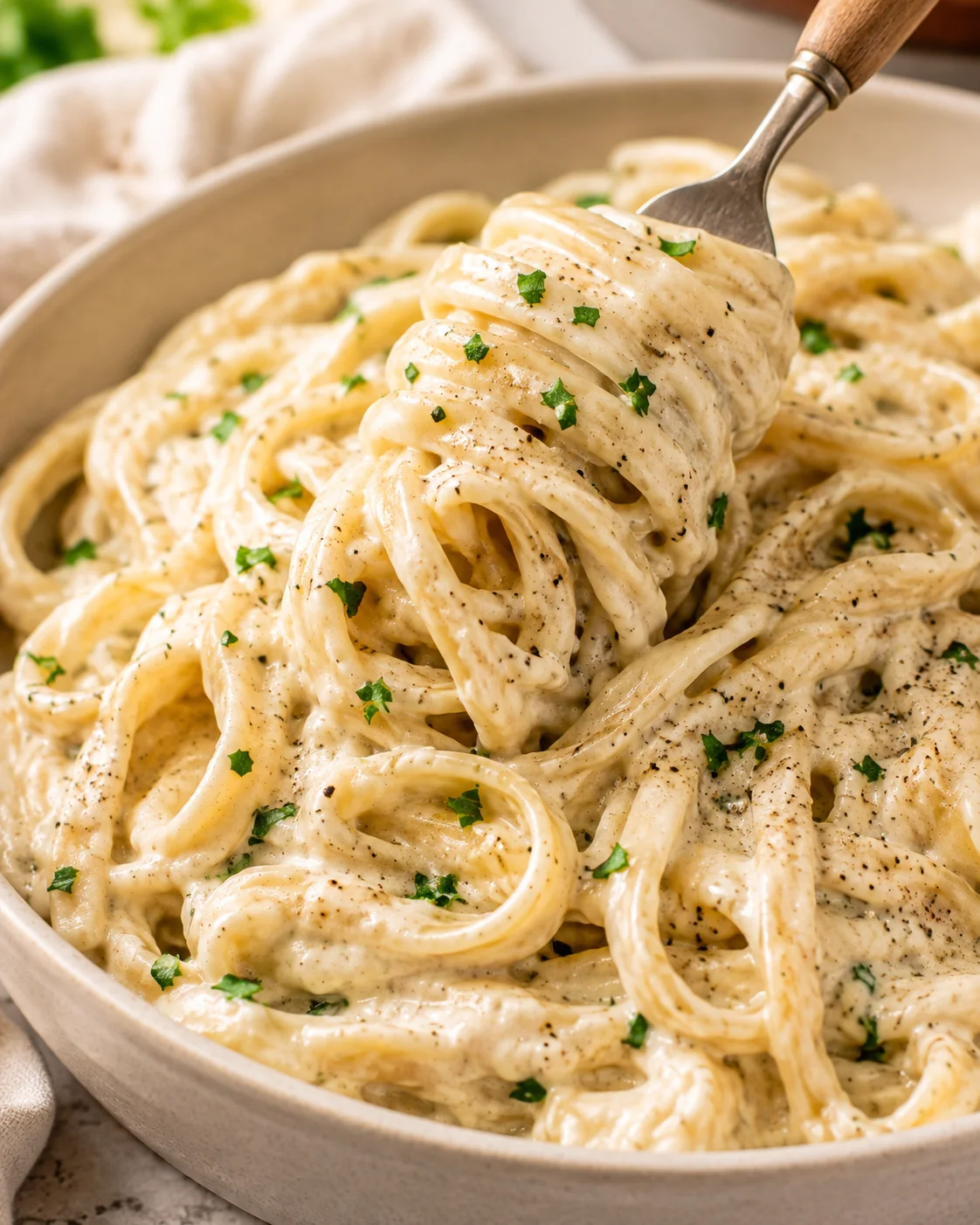 Bowl of cottage cheese Alfredo pasta with creamy sauce and parsley, fork lifting a twirl