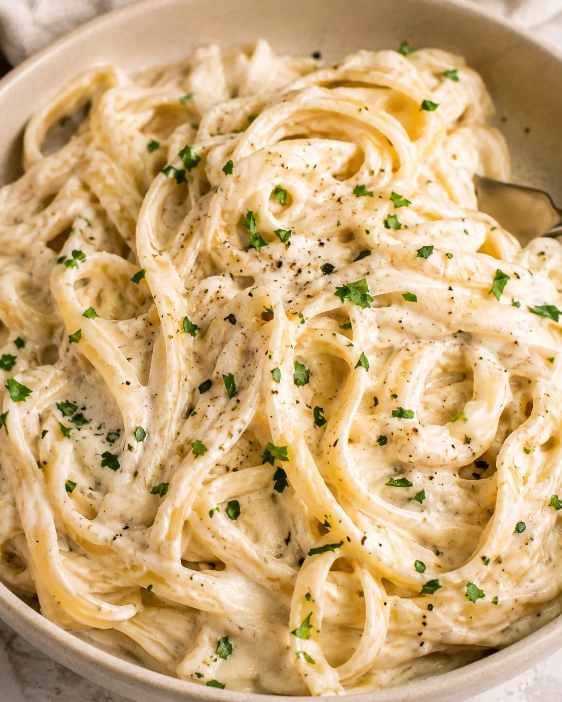 Close-up top view of creamy cottage cheese Alfredo pasta garnished with parsley and black pepper