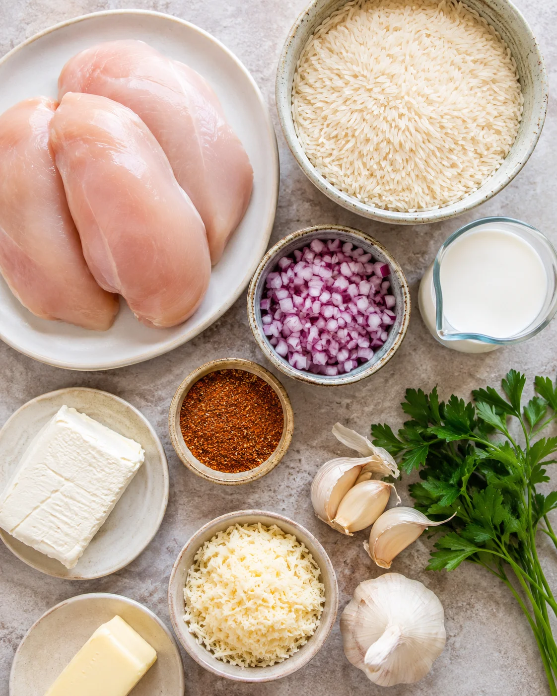 Top-down view of raw chicken breasts, rice, spices, dairy, garlic and parsley arranged