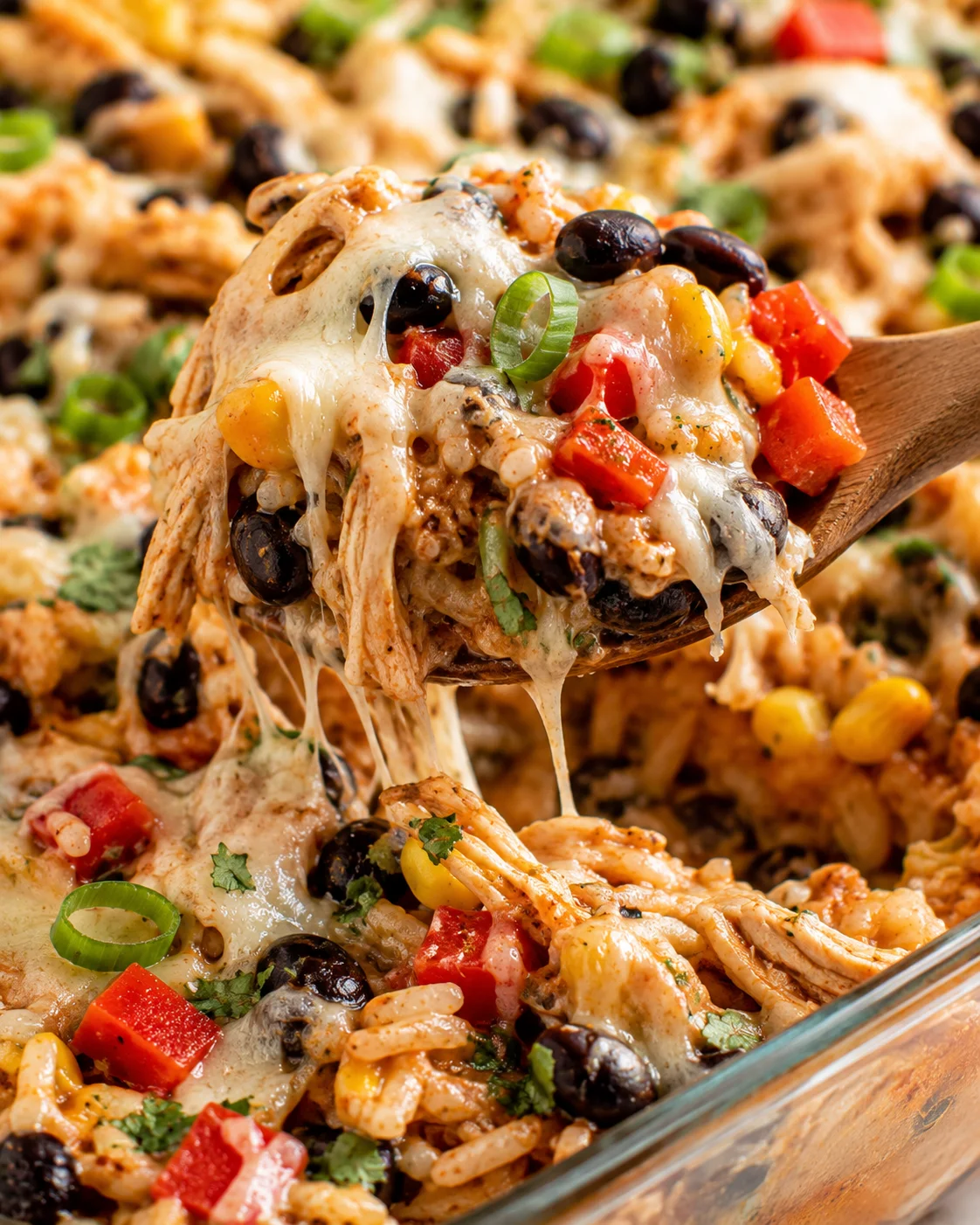 Wooden spoon lifting a cheesy forkful of chicken burrito casserole showing rice, beans, shredded chicken and melted cheese