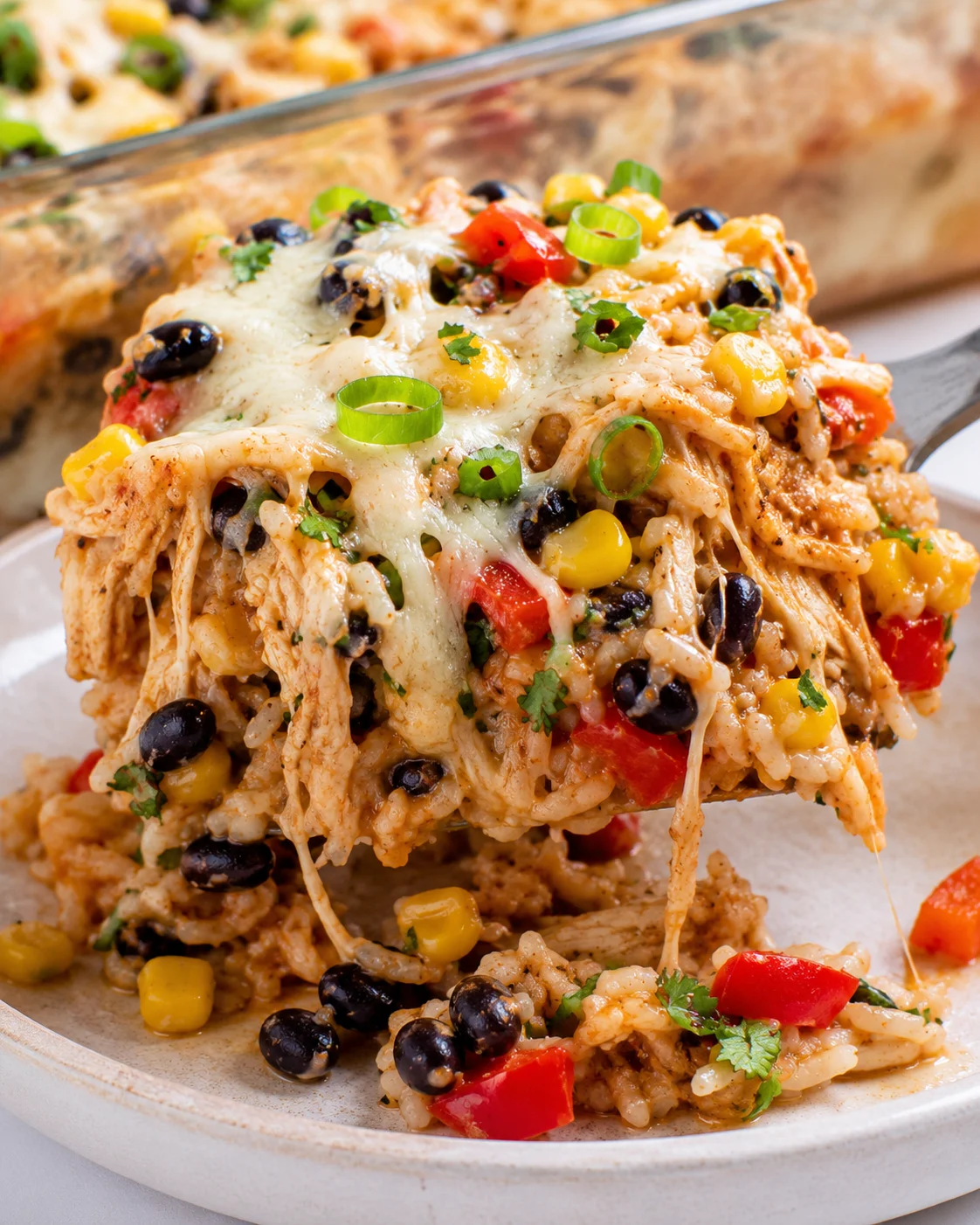 Plated scoop of chicken burrito casserole on a spatula with cheese stretching and the baking dish blurred in the background
