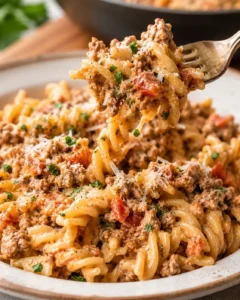 Fork lifting a bite of creamy ground beef pasta from a plated serving