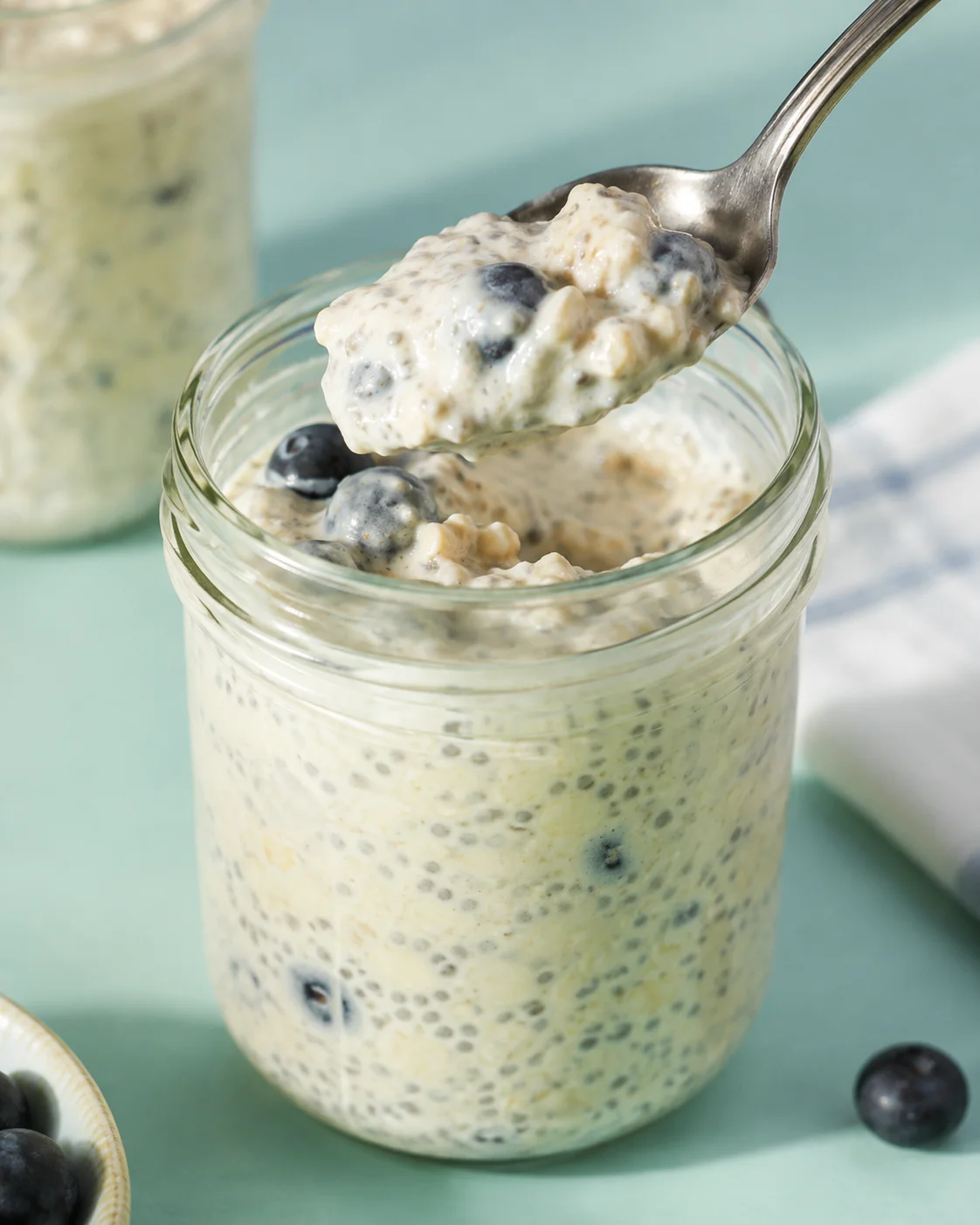 Spoon lifting a spoonful of easy overnight oats with blueberries from a jar
