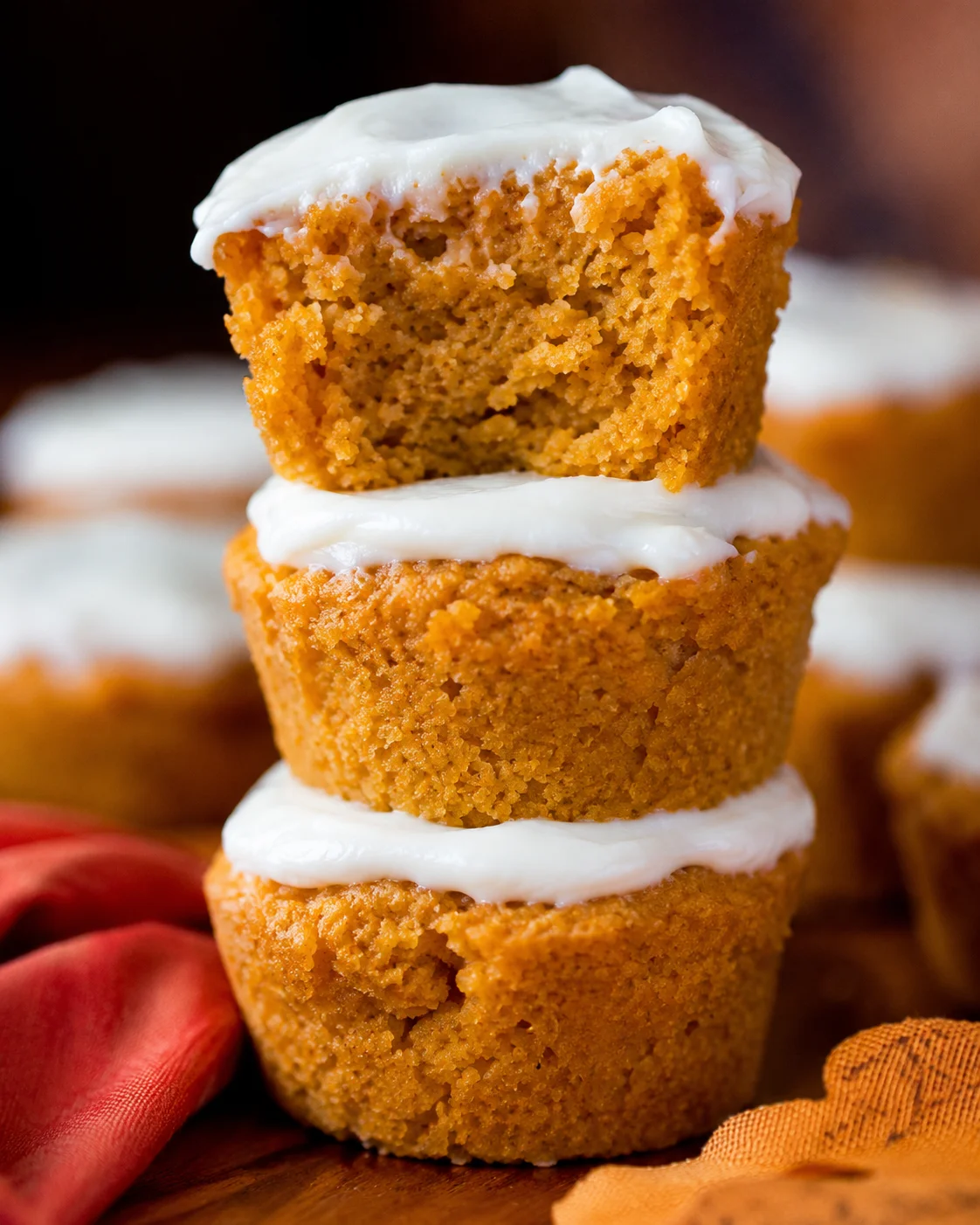 Stacked flourless pumpkin muffins with white frosting and a bitten top showing the interior crumb
