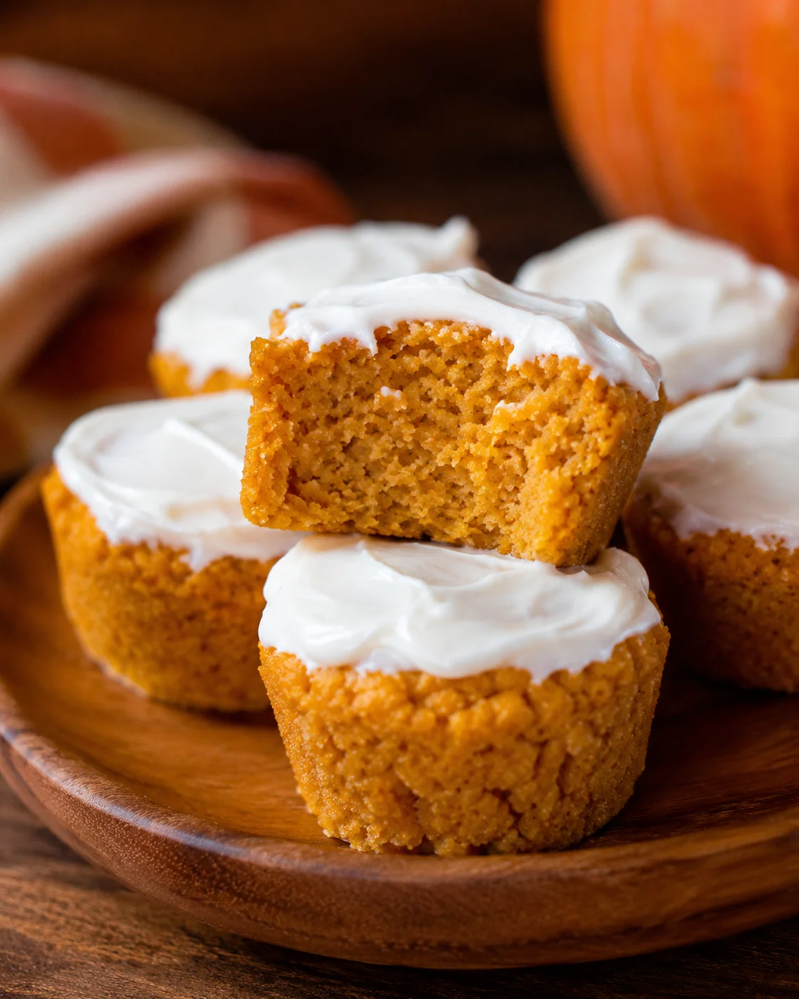 Several frosted flourless pumpkin muffins on a wooden plate with one muffin showing a bitten interior