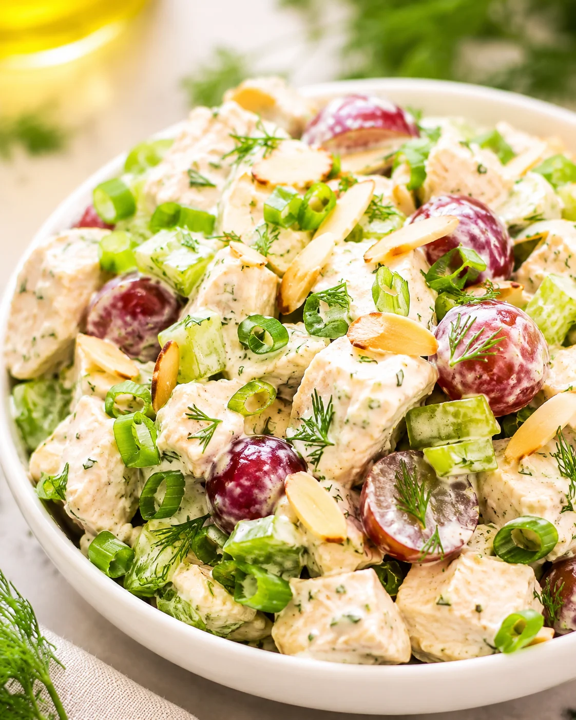 Bowl of Greek yogurt chicken salad with grapes, celery, dill, and sliced almonds