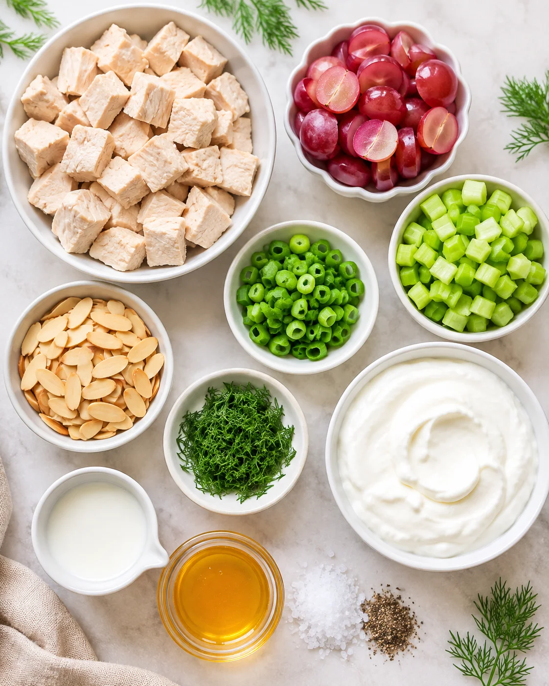Top-down layout of ingredients for Greek yogurt chicken salad including cubed chicken, grapes, celery, green onions, almonds, dill, yogurt, milk and honey