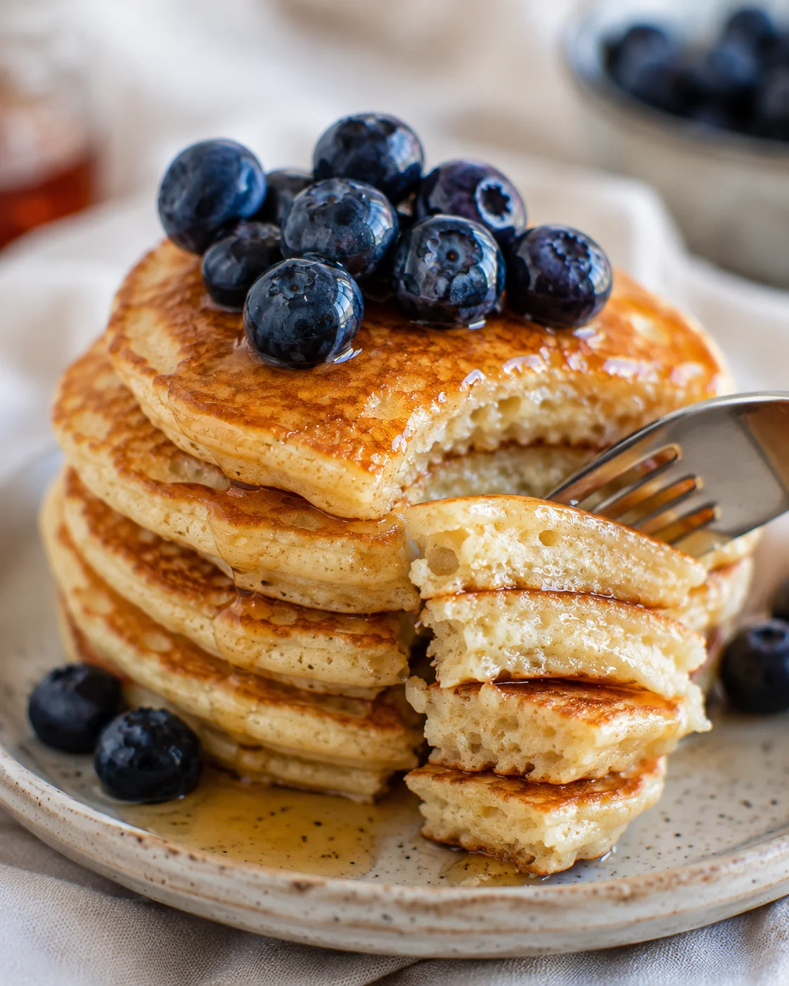 Fork lifting a bite from a stack of fluffy Greek yogurt pancakes topped with blueberries and syrup