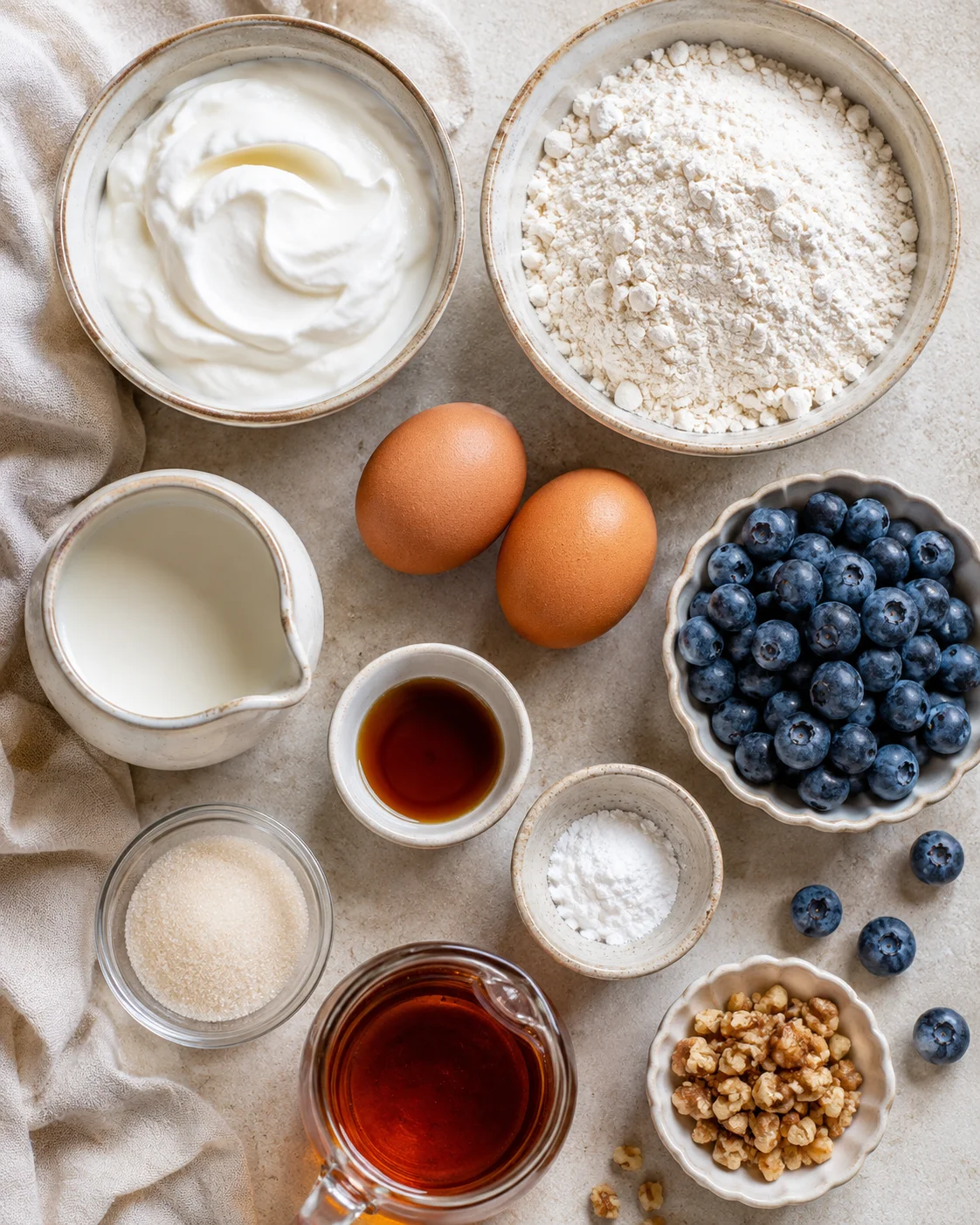Top-down view of ingredients for Greek yogurt pancakes including yogurt, flour, eggs, milk, blueberries and maple syrup