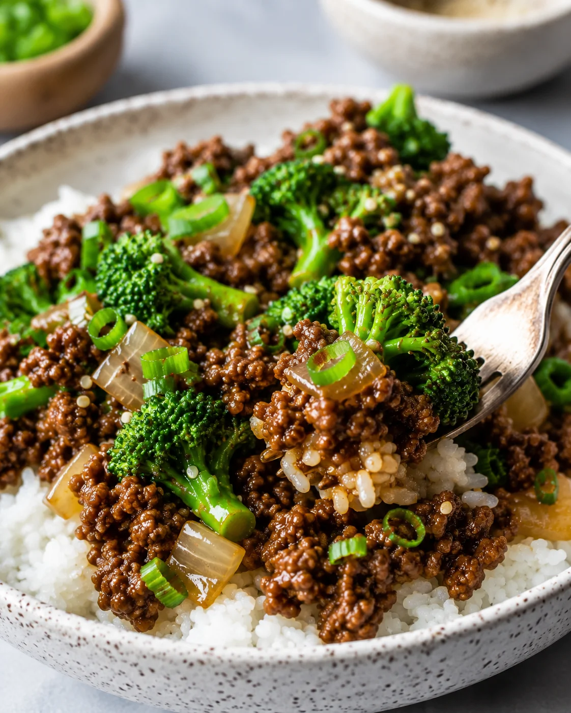 Side view of ground beef and broccoli stir fry with a forkful lifted from a bowl