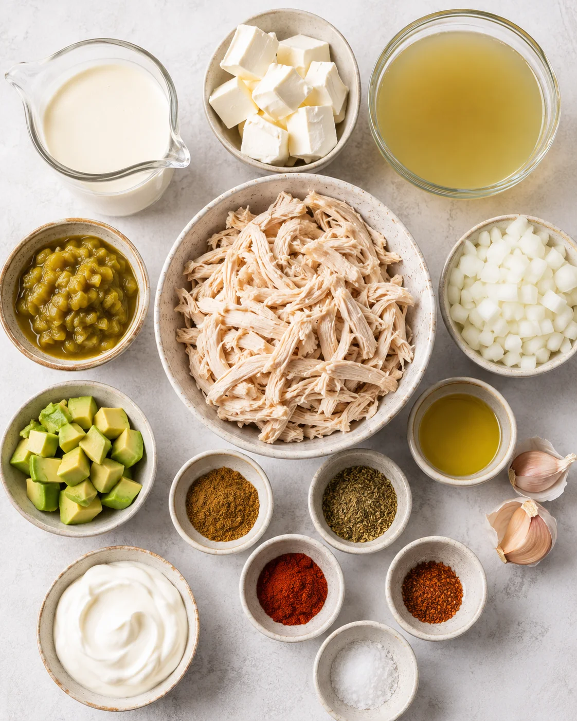 Top-down arrangement of ingredients for keto white chicken chili including shredded chicken, cream cheese, cream, green chiles, onion, avocado and spices