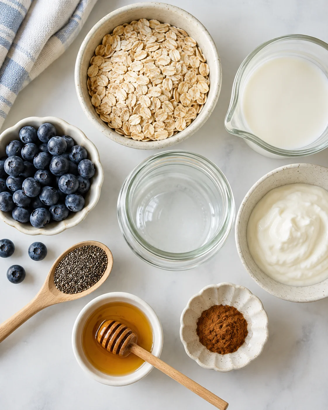 Top-down view of ingredients for easy overnight oats in bowls including oats, milk, yogurt, blueberries, chia seeds, honey and cinnamon