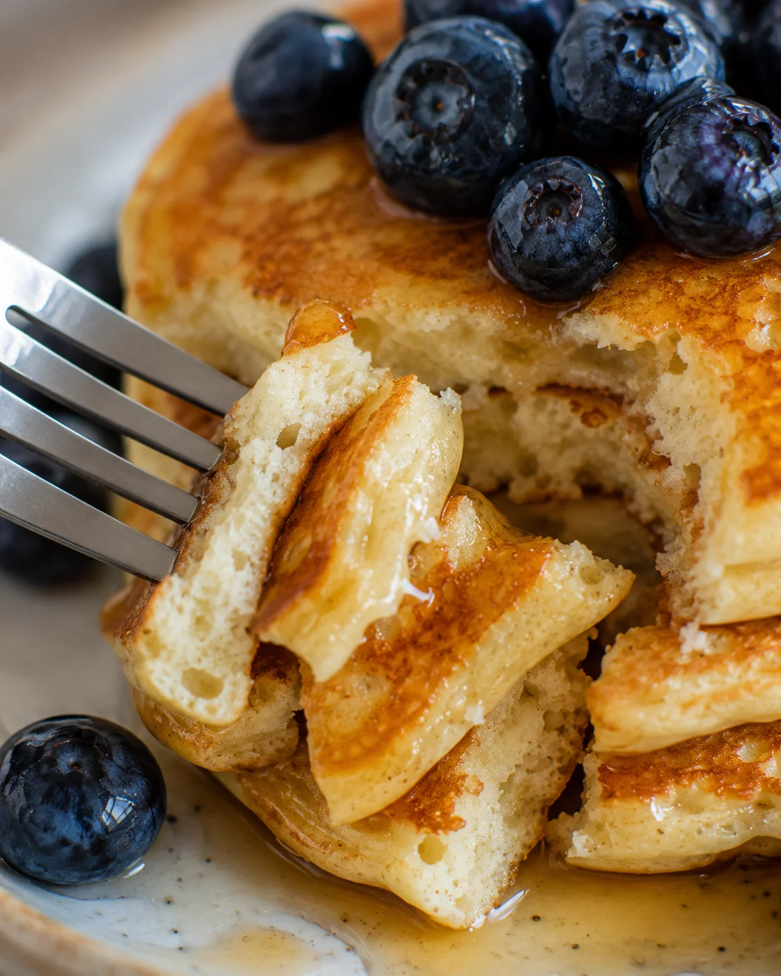Close-up of fluffy Greek yogurt pancake interior on a fork with syrup and blueberries nearby