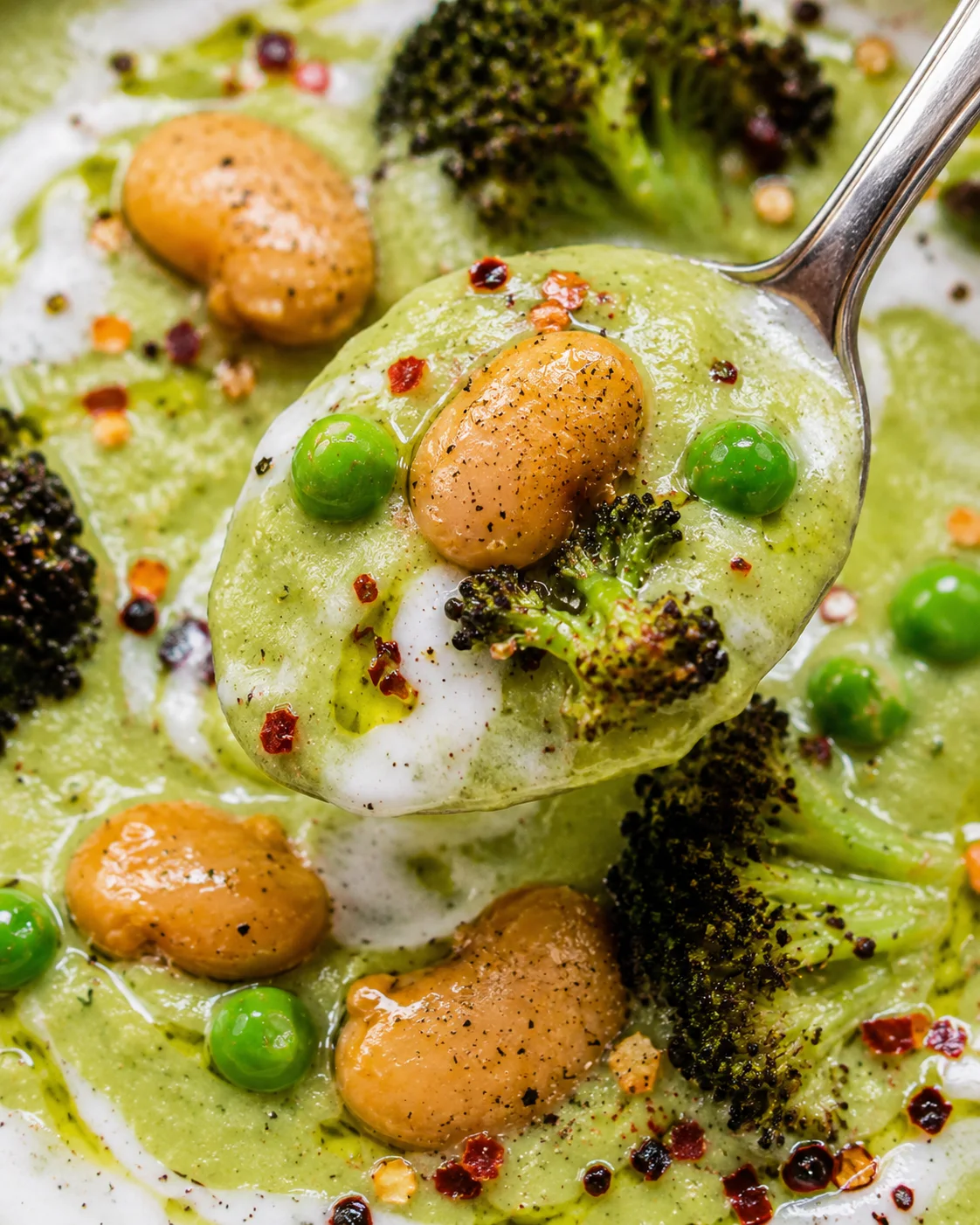 Close-up of vibrant green soup with beans, broccoli, and coconut yogurt on a spoon.