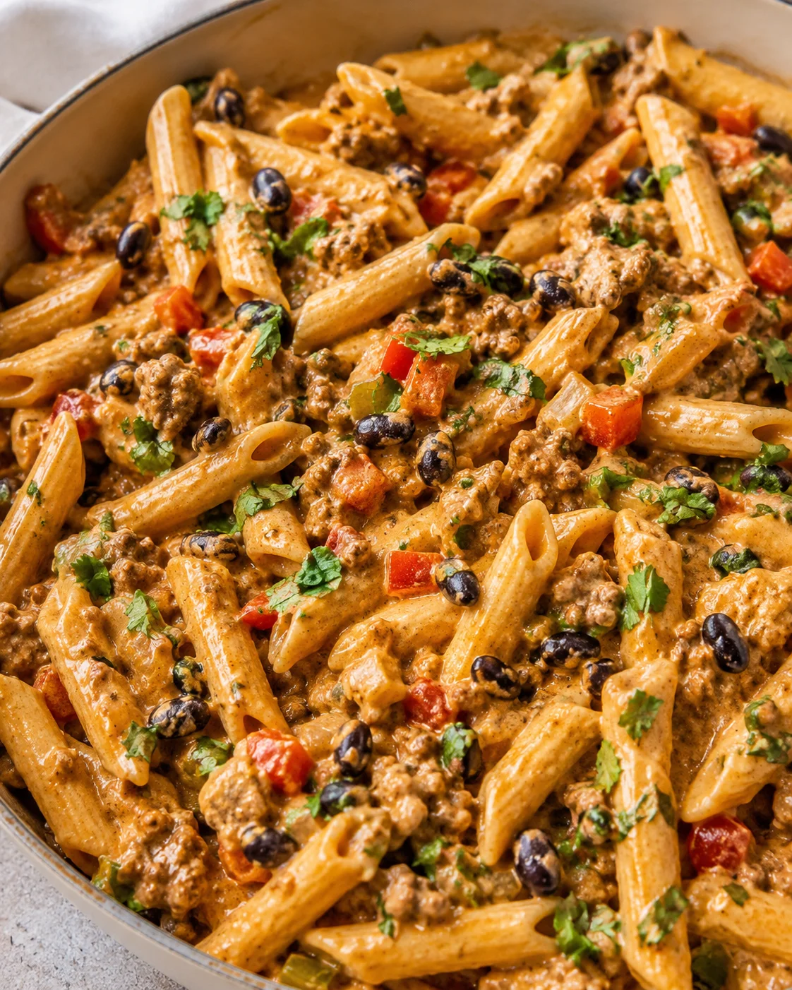 Close-up of creamy taco pasta with seasoned beef, black beans, and fresh herbs