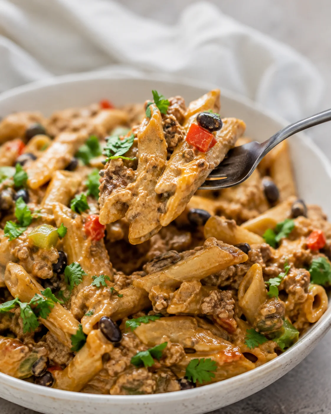 Close-up of creamy taco pasta with vegetables and black beans in a white bowl