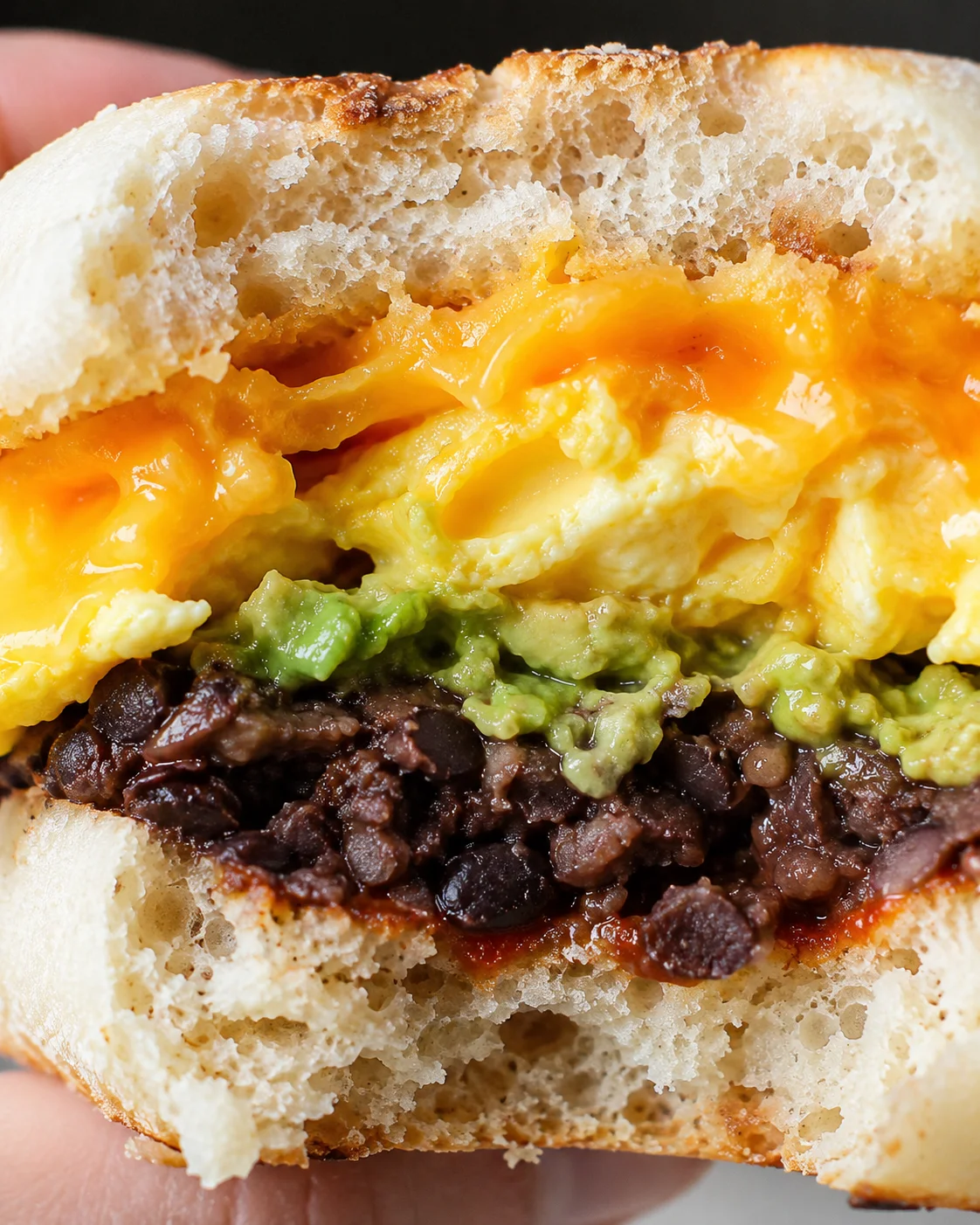 Close-up of a hearty protein breakfast sandwich with eggs, beans, and avocado