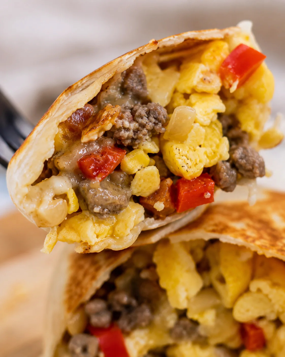 Close-up of a delicious, filled breakfast burrito with eggs, sausage, and vegetables.