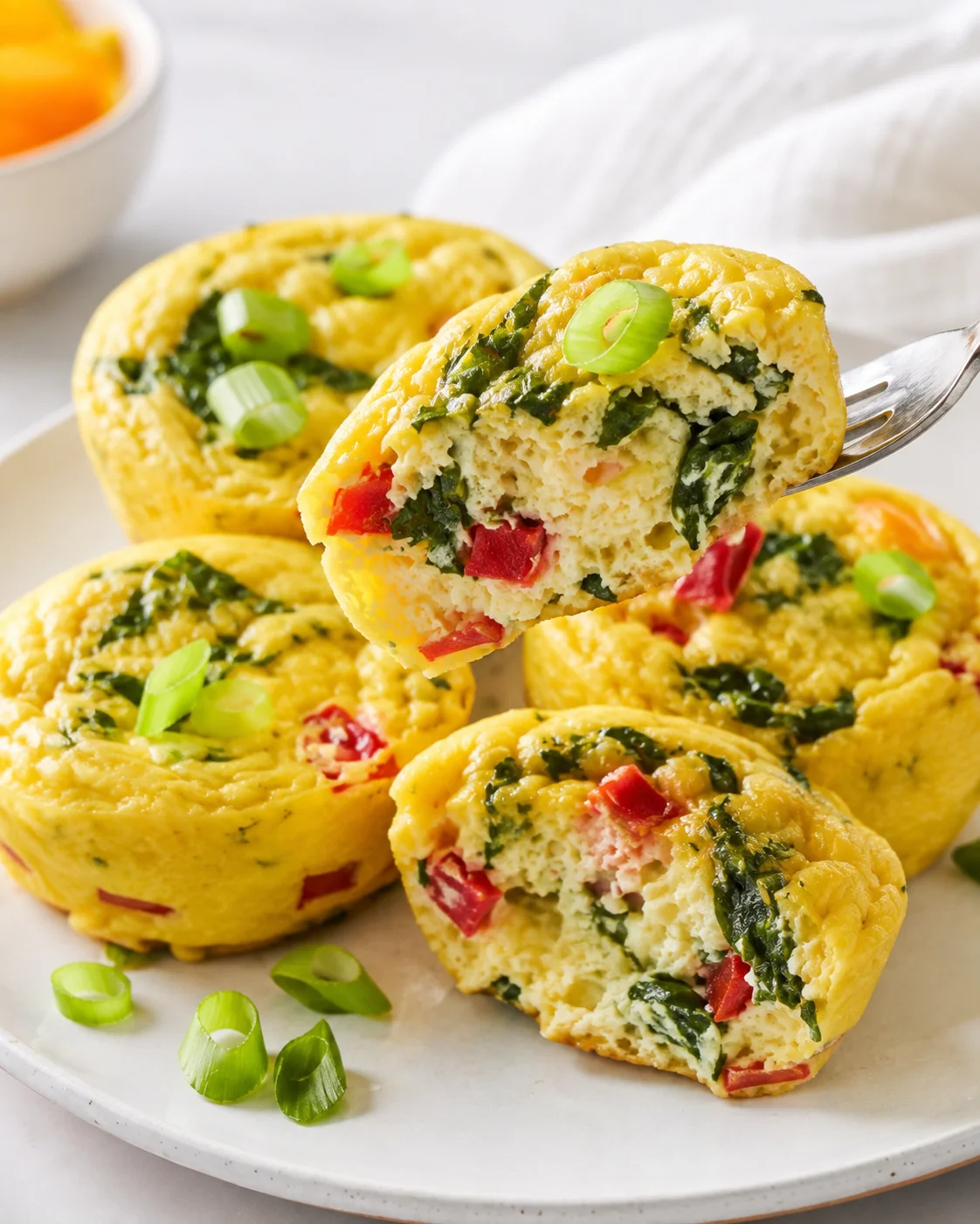 Golden savory egg muffins with spinach, red peppers, and green onions on a white plate.