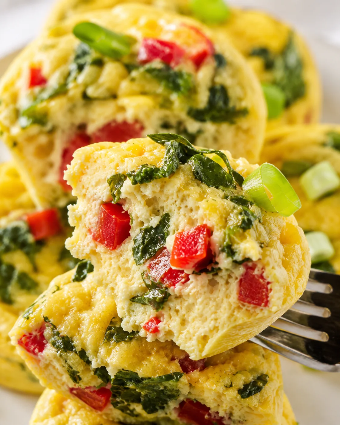 Close-up of a fluffy spinach and red pepper frittata slice on a fork.