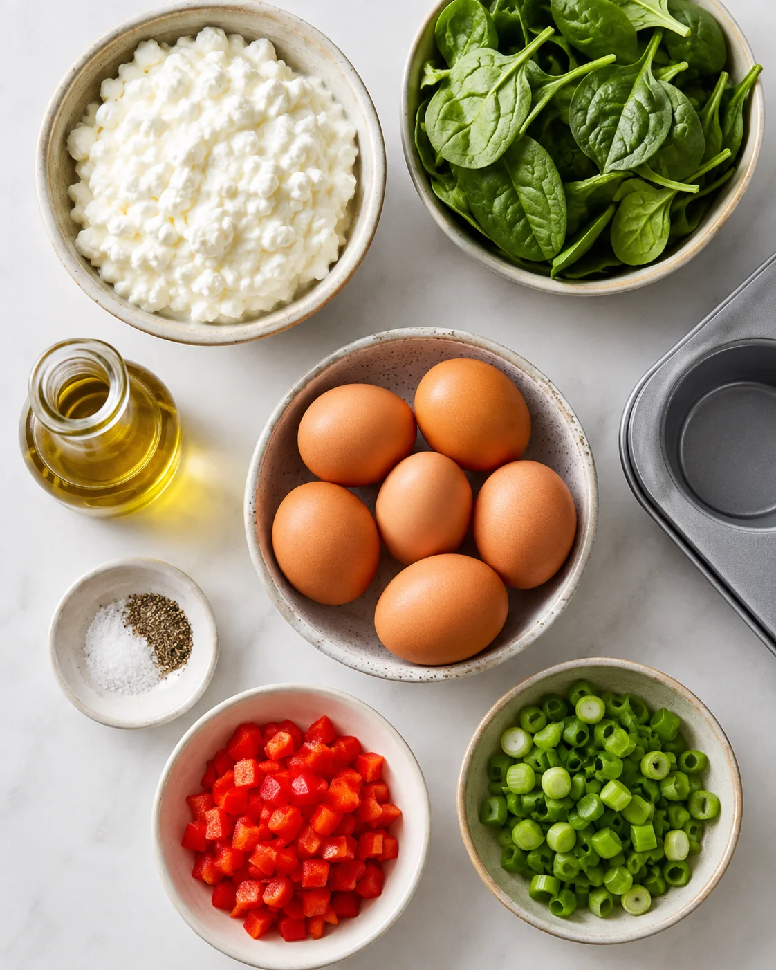 Top-down view of eggs, ricotta, spinach, bell pepper, green onions, olive oil, and salt on a marble counter.