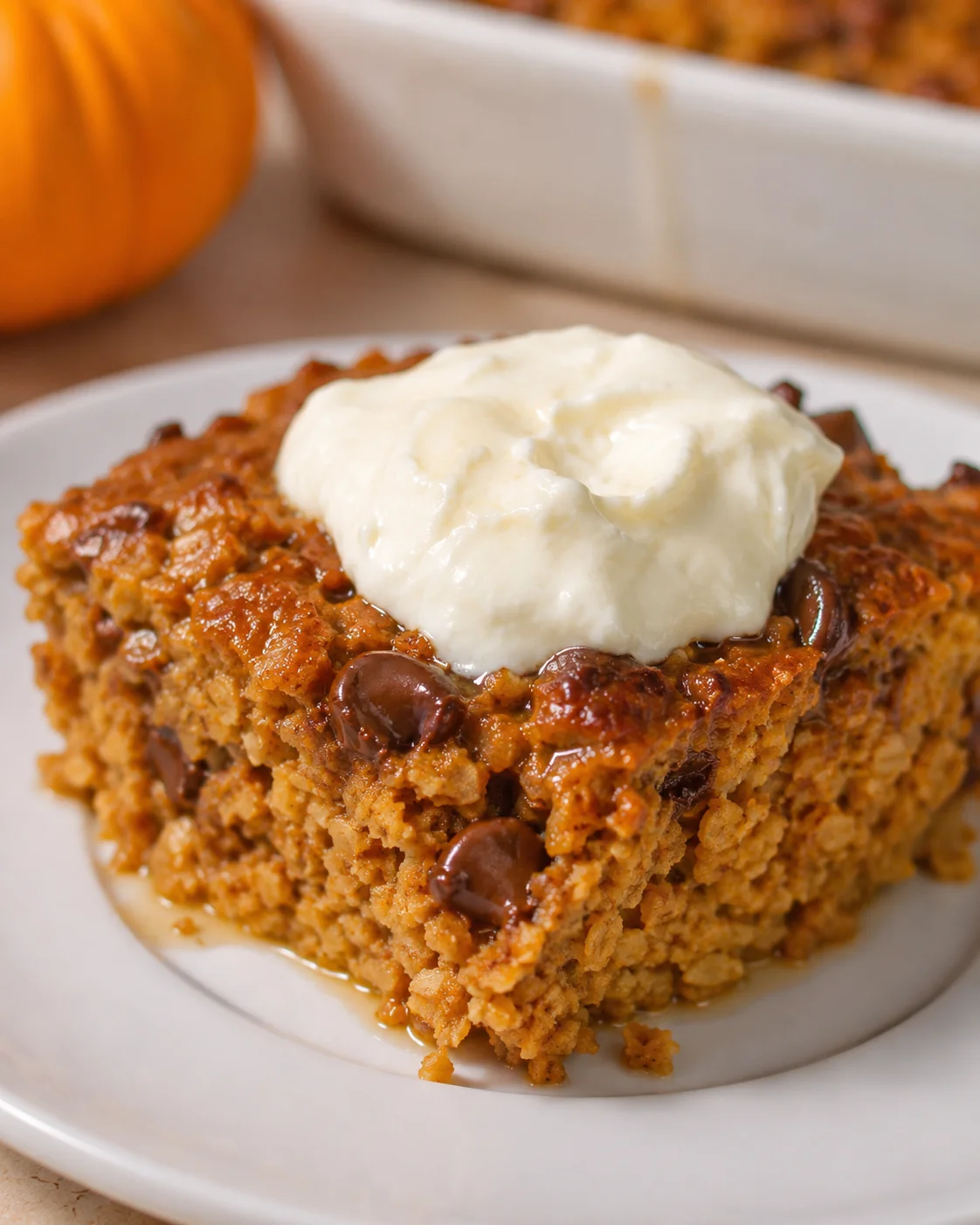 Square slice of pumpkin-spice crumb cake topped with cream cheese frosting on a white plate.