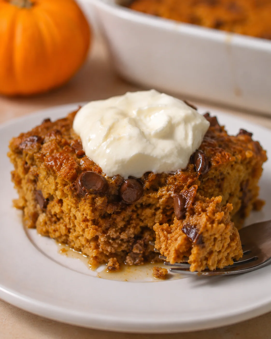 Slice of pumpkin loaf with chocolate chips topped with cream cheese frosting on a white plate.
