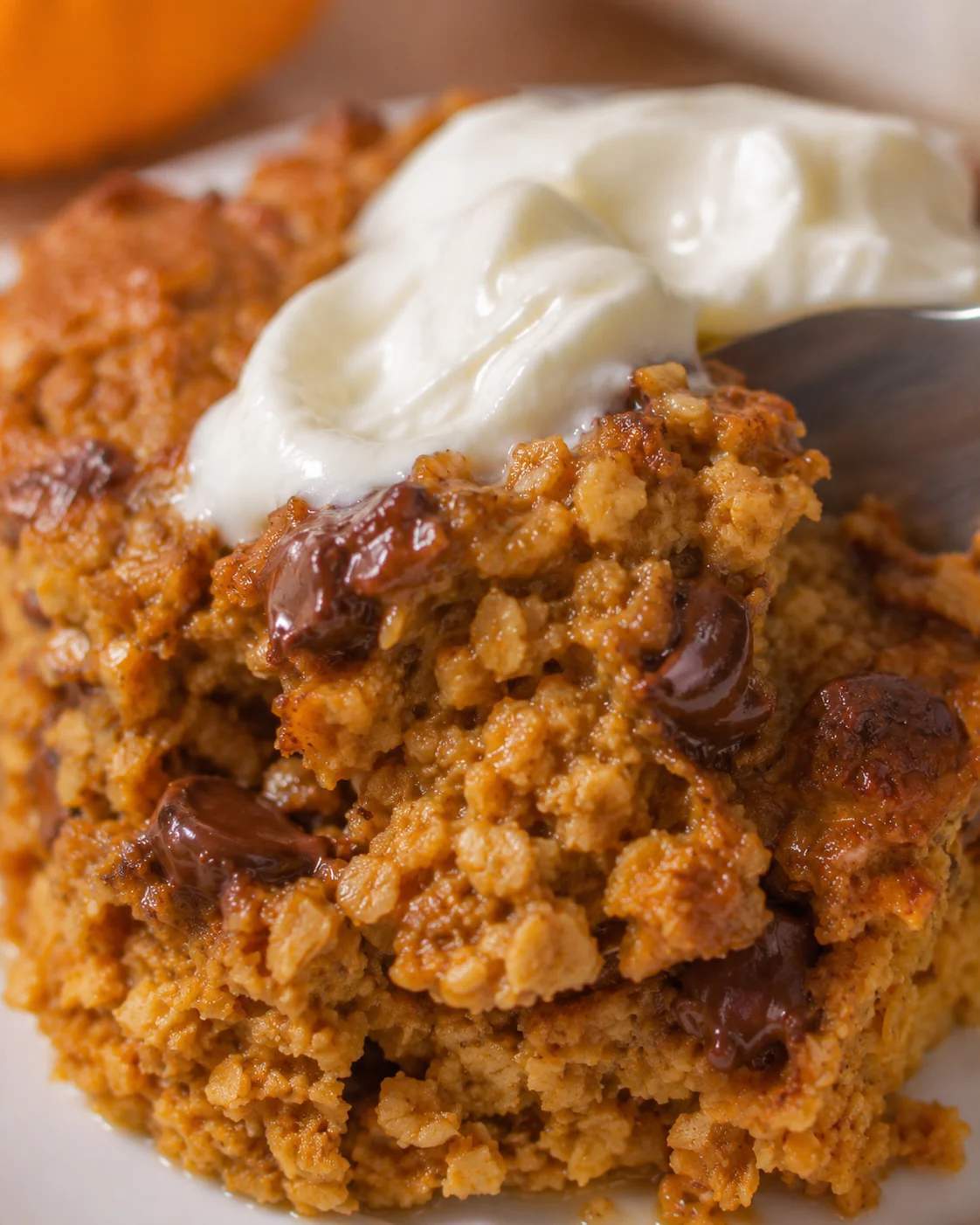 Close-up of a warm cherry crumble topped with whipped cream on a white plate.