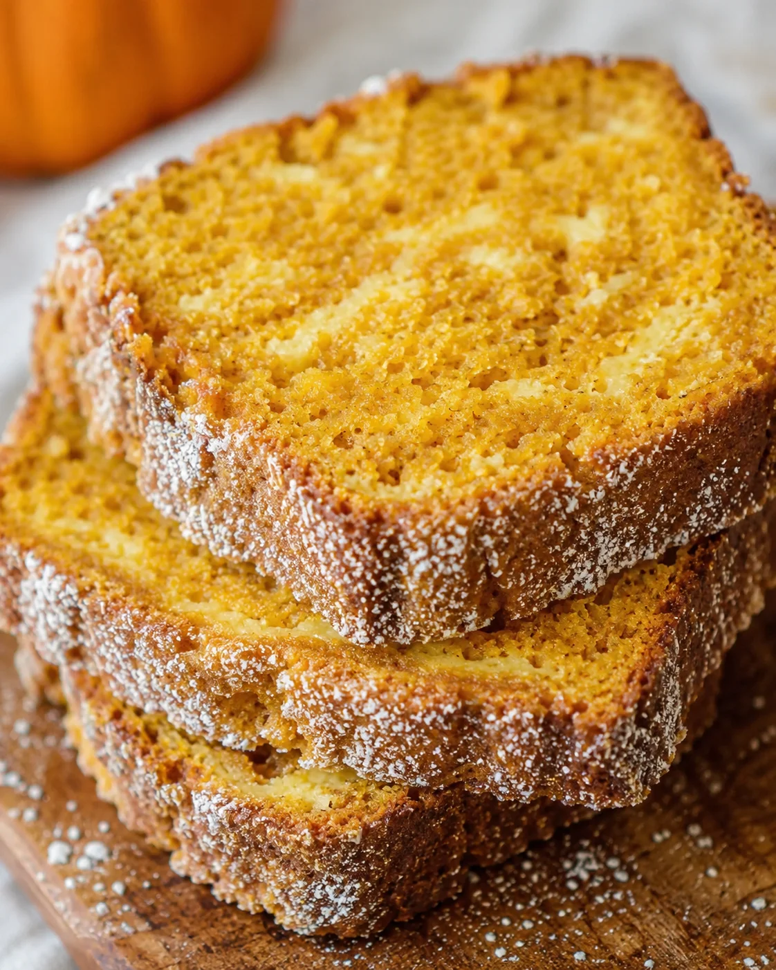 Stacked slices of pumpkin-spice bread with a sugared crust on a wooden board.