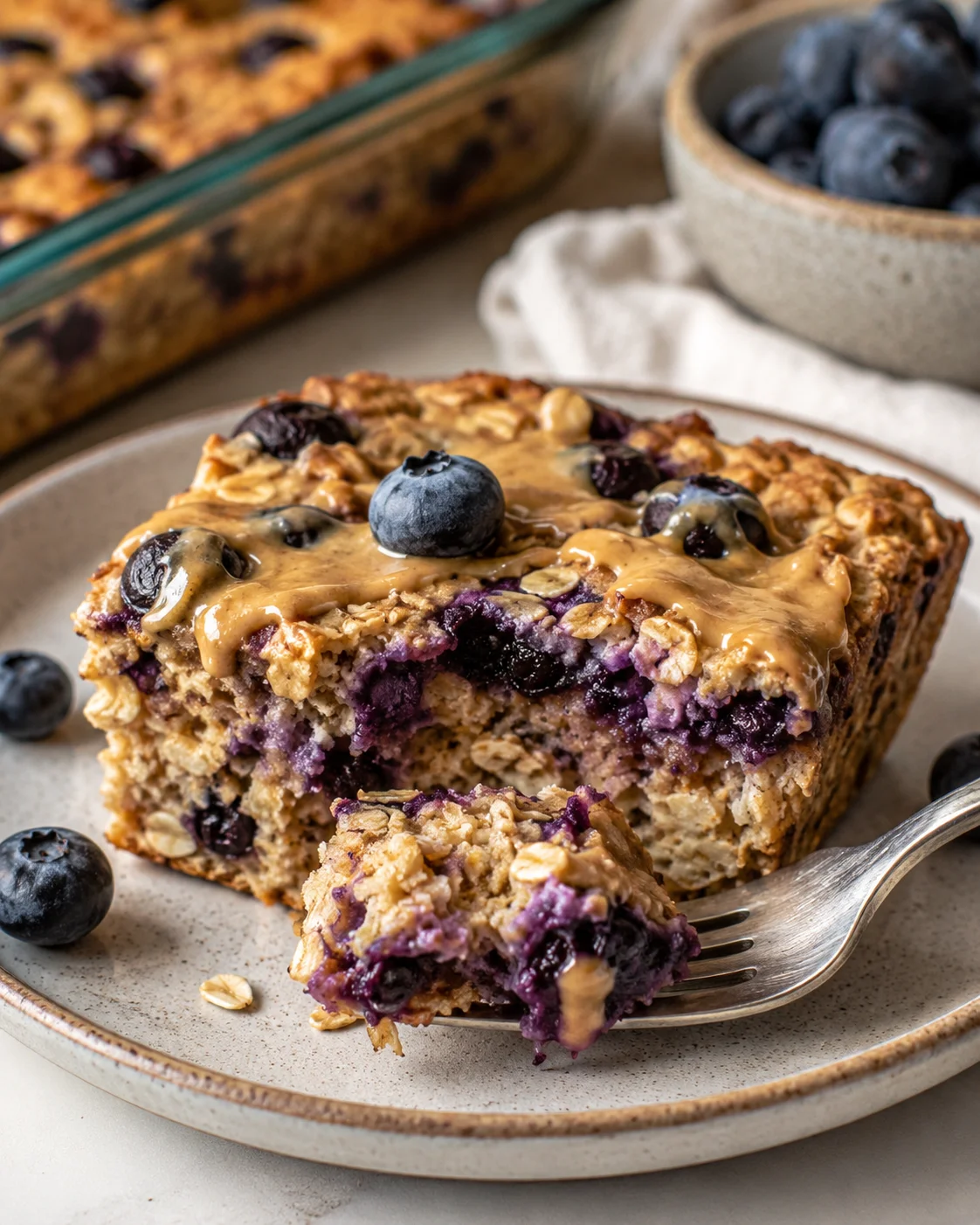 slice of blueberry oat bar with caramel glaze on a beige plate, fresh blueberries nearby