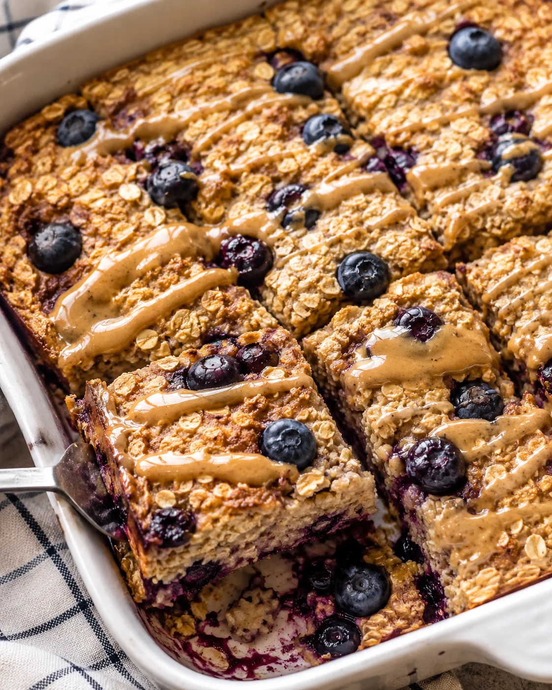 blueberry oat crumble bars sliced in a white baking dish with drizzled caramel