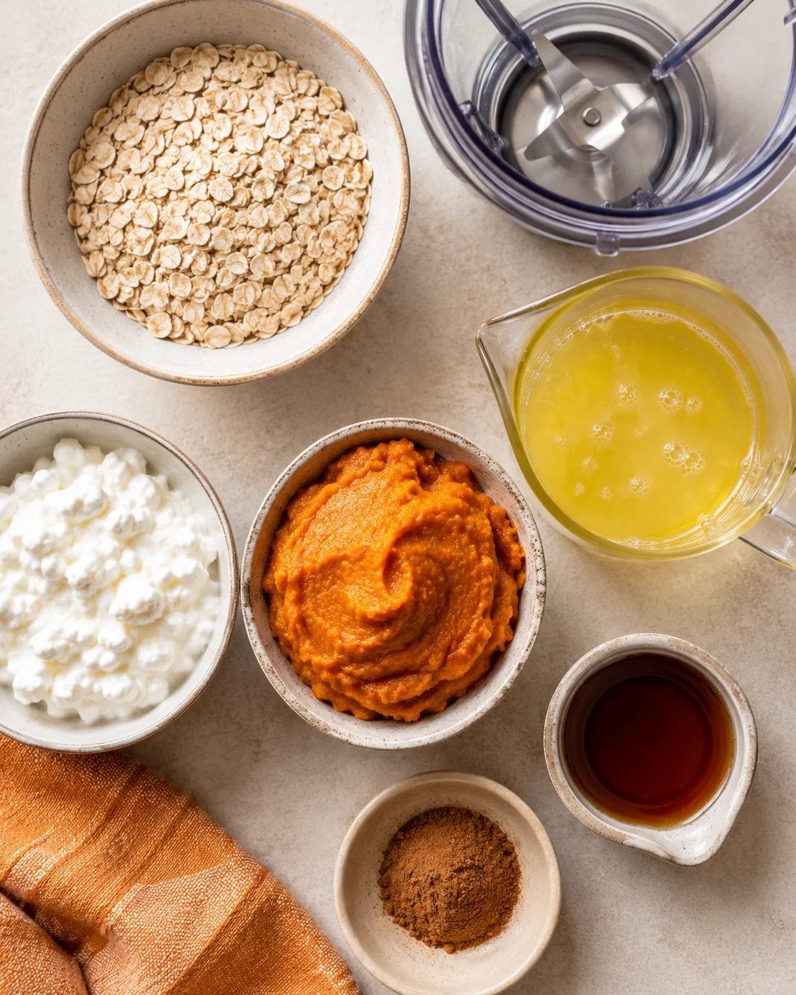 Overhead view of oats, yogurt, pumpkin puree, and pale yellow liquid in a measuring jug.
