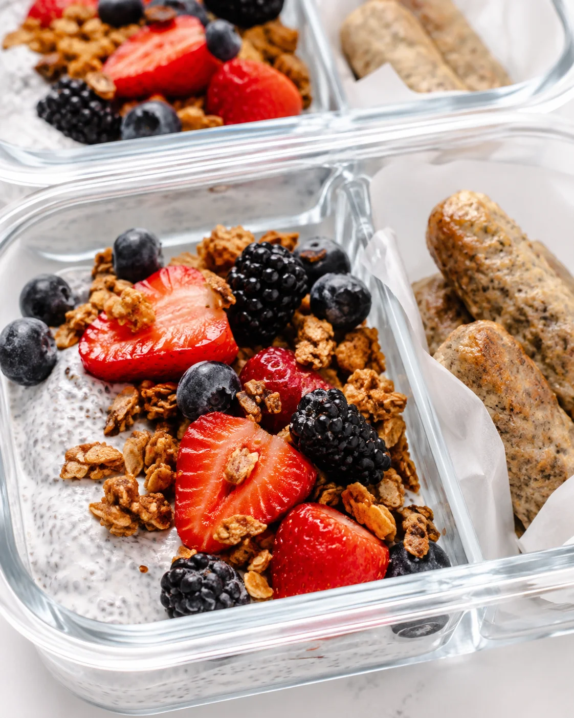 Glass meal-prep containers filled with chia yogurt topped with granola and fresh berries.