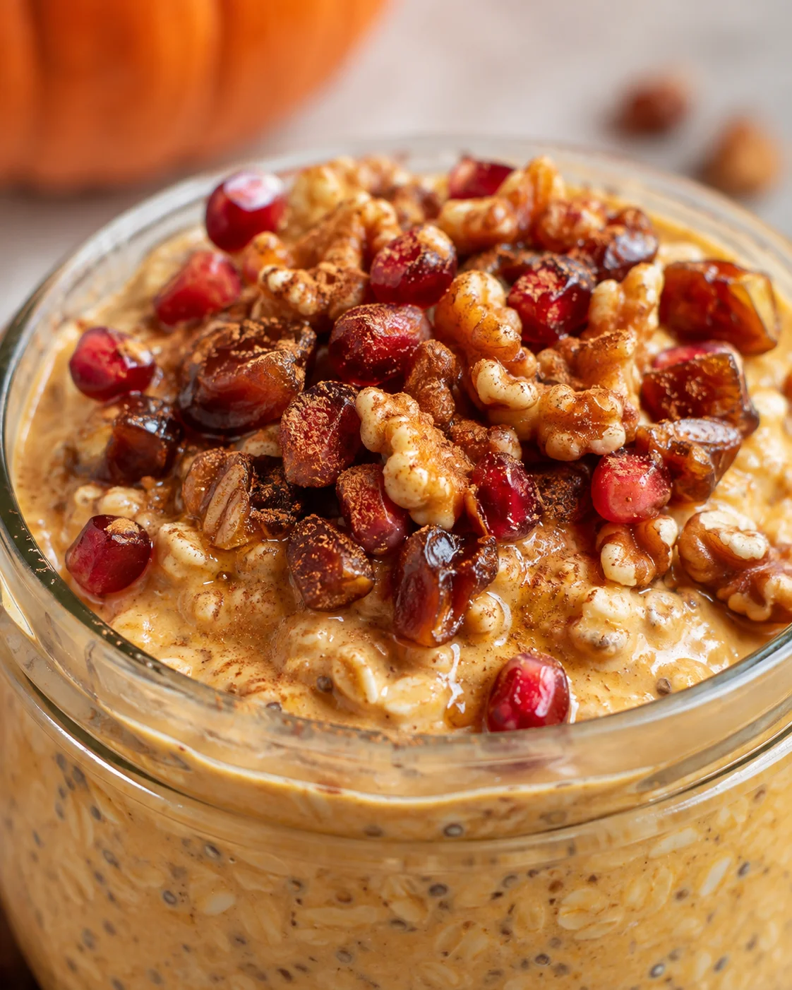 Glass mason jar of pumpkin-spiced overnight oats with chia seeds, topped with walnuts and cranberries.