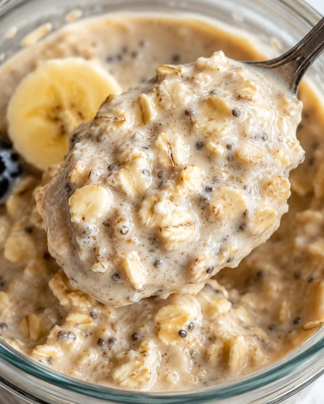 Close-up of a spoonful of creamy banana oatmeal with chia seeds in a glass bowl