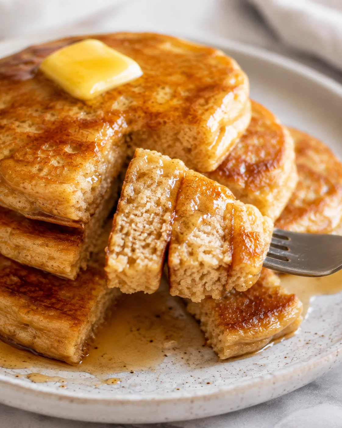 Stack of fluffy, golden-brown pancakes with a pat of butter on top, syrup pooling on a ceramic plate