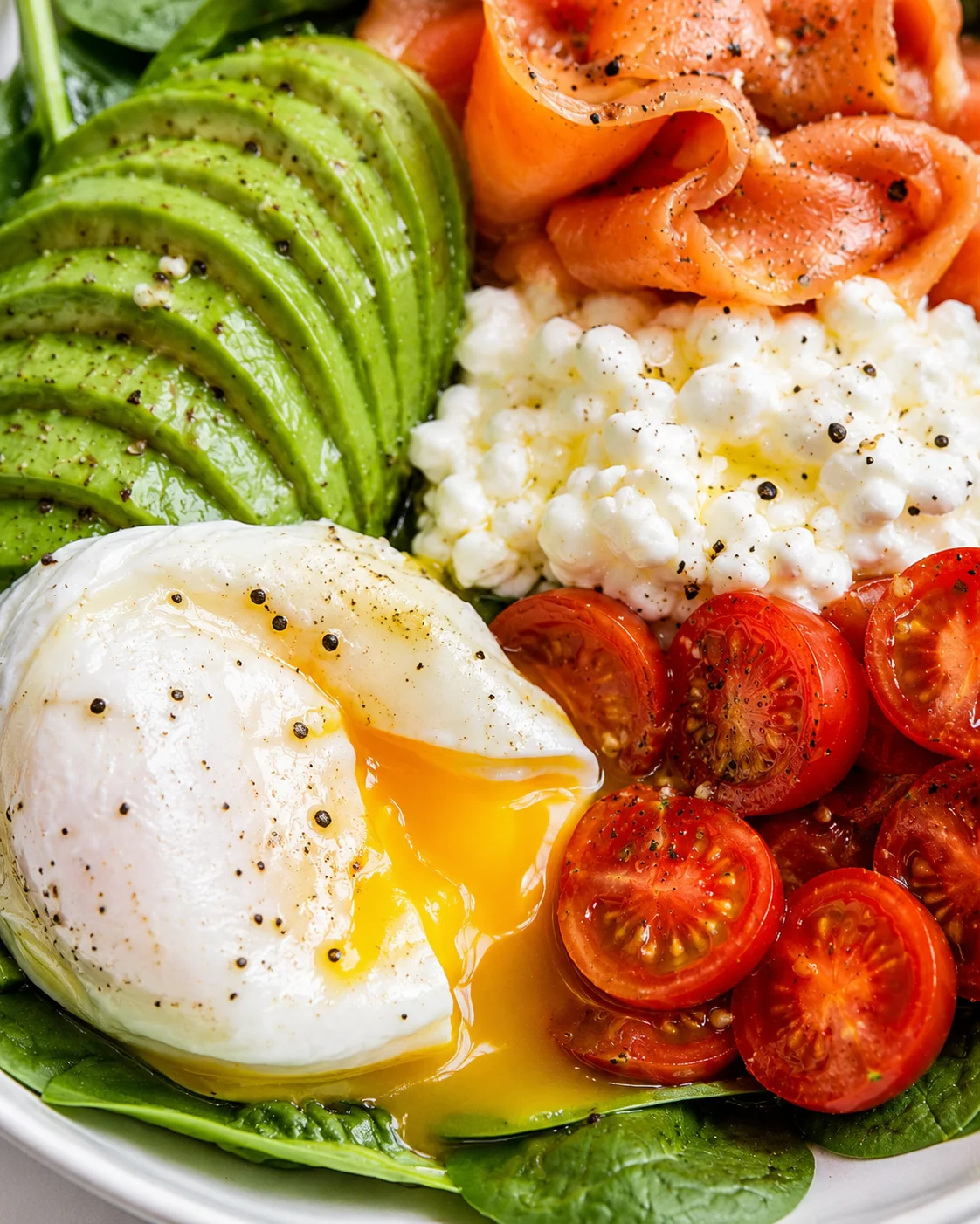 Close-up of a vibrant breakfast bowl with avocado, smoked salmon, poached egg, cottage cheese, and cherry tomatoes.