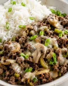 Close-up of Philly cheesesteak meal prep showing ground beef, mushrooms, peppers, melted cheese and basmati rice